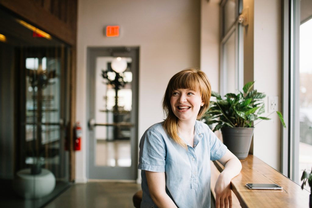 A woman is sitting at a counter, smiling while looking off to the side, in this guide for perimenopause and menopause hormone therapy by Lemonaid Health.
